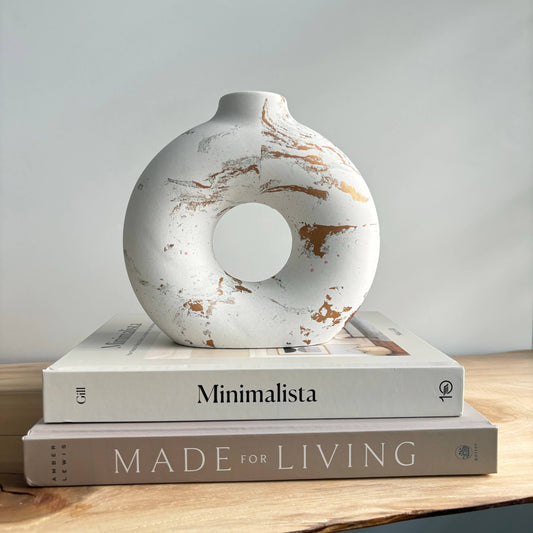 A modern concrete donut vase with white and gold color accents, displayed on top of two books titled 'Minimalista' and 'MADE FOR LIVING'.